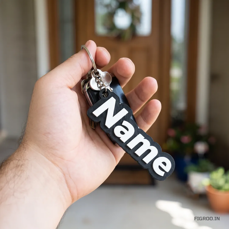 A person holding a customized 3D printed name keychain in black and white attached to car keys, standing in front of a house.